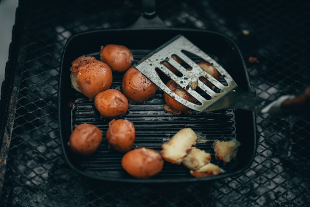 在铸铁煎锅中还处于烹饪阶段的年轻炸土豆被烤好，并用铲子压紧图片下载