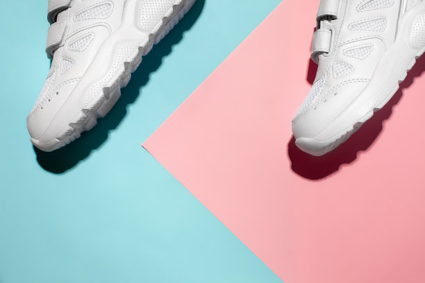 顶视图两白色运动鞋在一个精致的几何纸粉红色和蓝色的背景与硬阳光，文本复制空间图片下载