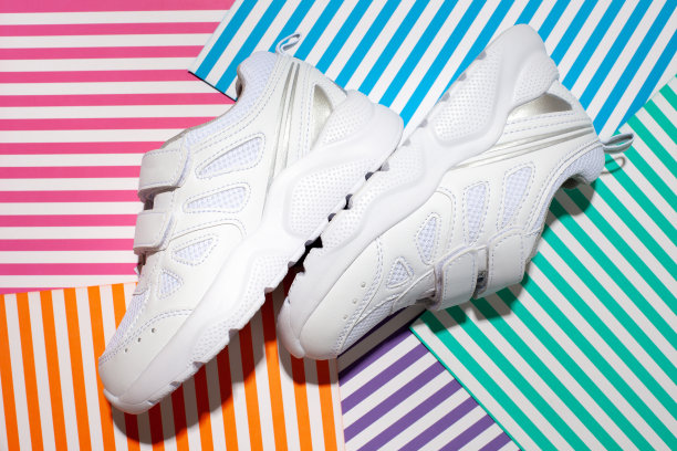 顶视图两个白色的小孩运动鞋与尼龙搭扣为舒适的鞋在抽象的几何纸上彩色条纹背景与硬阳光图片下载