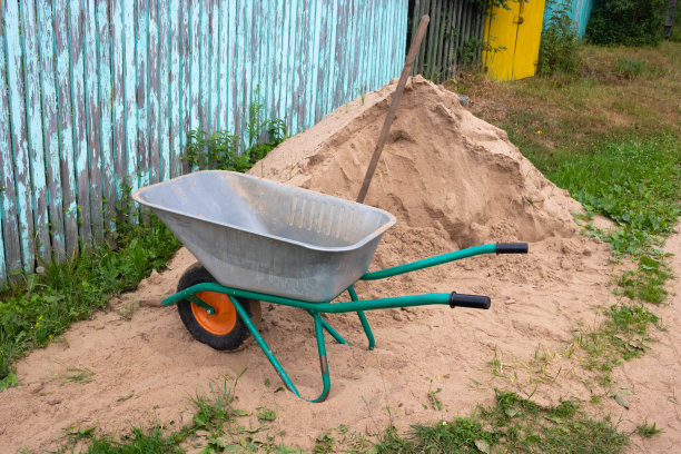 一辆施工车和一把铲子，旁边是一堆沙子和一个蓝色的旧栅栏图片下载