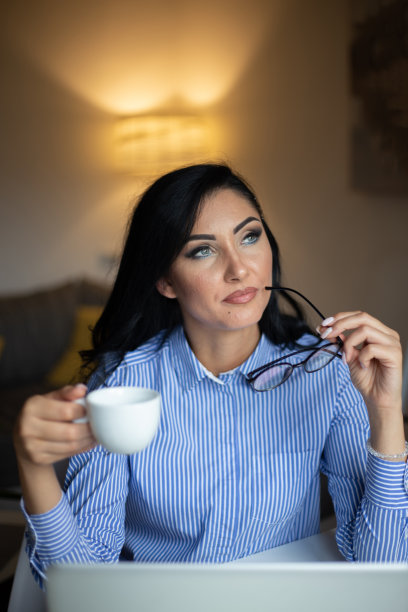年轻女子享受她的咖啡，而工作或学习笔记本电脑在家庭办公室库存照片图片下载