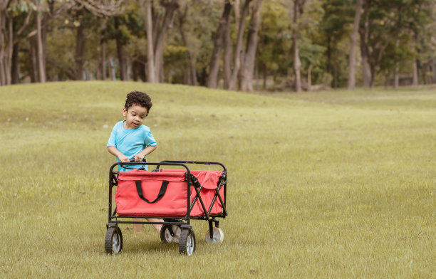 肖像小可爱可爱的非洲男孩学习，做活动，快乐地玩耍，坐在红色的手推车在室外花园在暑假与复印空间。教育的概念。图片下载