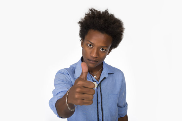 年轻的黑人男子与非洲发式穿蓝色衬衫在孤立的白色背景做快乐的拇指向上的手势与手。图片下载