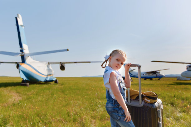 一个小女孩提着一个手提箱站在飞机附近的停机坪上。她要去旅行图片下载