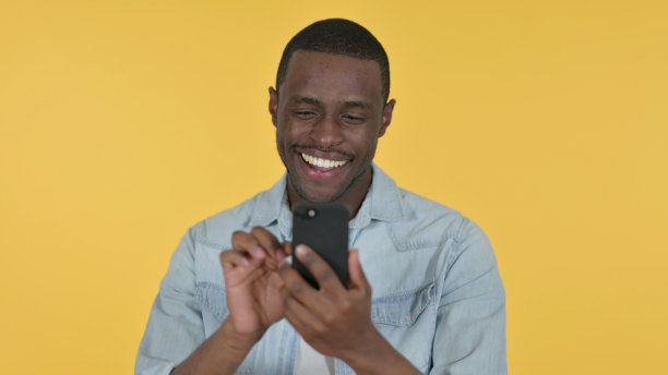 年轻的非洲男子使用黄色背景的智能手机图片下载