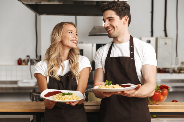 兴奋的年轻朋友爱夫妇厨师在厨房拿着盘子美味的食物。图片下载