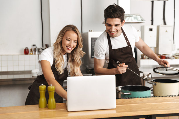 感情丰富的年轻朋友们在厨房里用笔记本电脑烹饪。图片下载