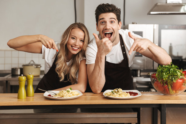 兴奋的年轻朋友爱夫妇厨师在厨房吃美味的意大利面竖起大拇指。图片下载