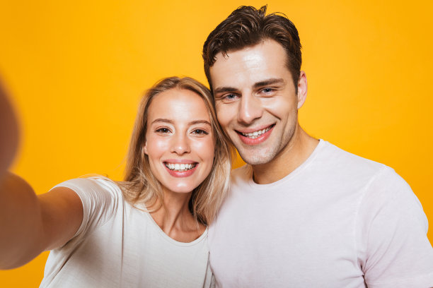 一对相爱的情侣站在黄色墙的背景下自拍。图片下载