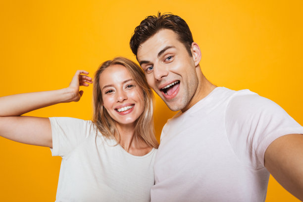 一对情侣孤立地站在黄色的墙壁上，用相机自拍。图片下载