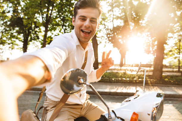 兴奋的年轻商人踏着滑板车在户外用相机自拍。图片下载