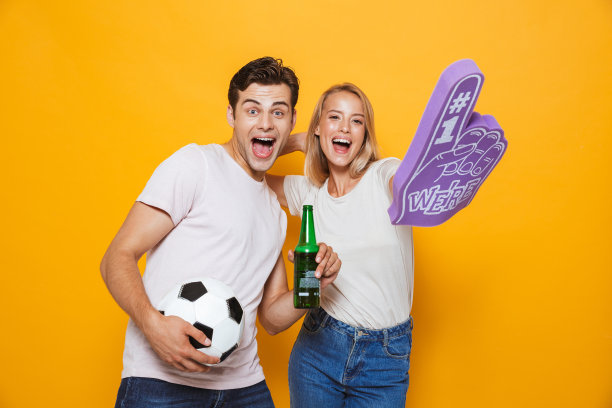 一对年轻情侣戴着头号球迷手套，手里拿着足球和啤酒。图片下载