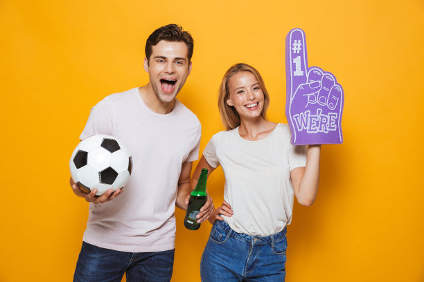 一对年轻情侣戴着头号球迷手套，手里拿着足球和啤酒。图片下载