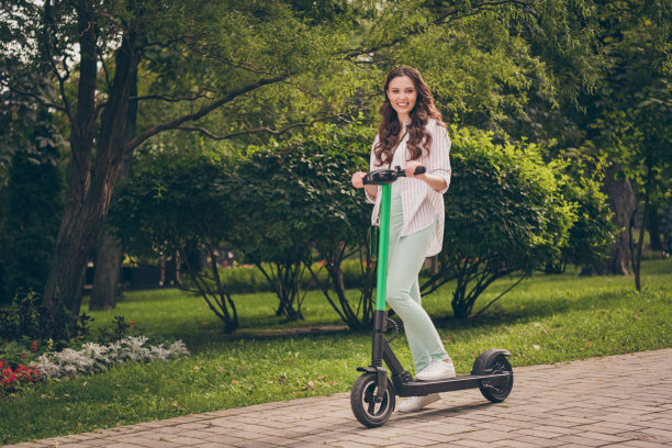 全身照片迷人的年轻活泼的女孩骑电动车快乐的微笑乐趣在公园绿树自然图片下载