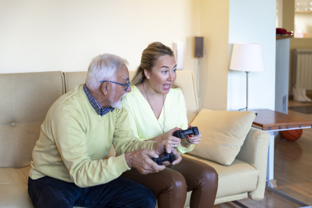 微笑的中年妇女和她的父亲一起在家里玩电子游戏。图片下载