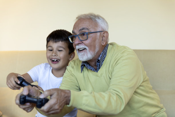 快乐的小朋友在家里玩电脑游戏的时候和爷爷玩得很开心。图片下载