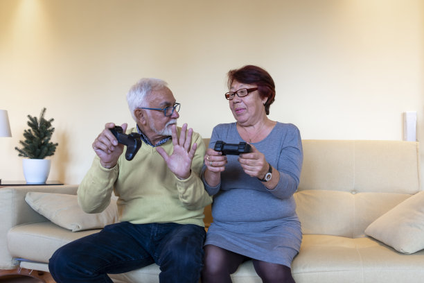 微笑的老人和他美丽的妻子在家里一起玩电子游戏。图片下载