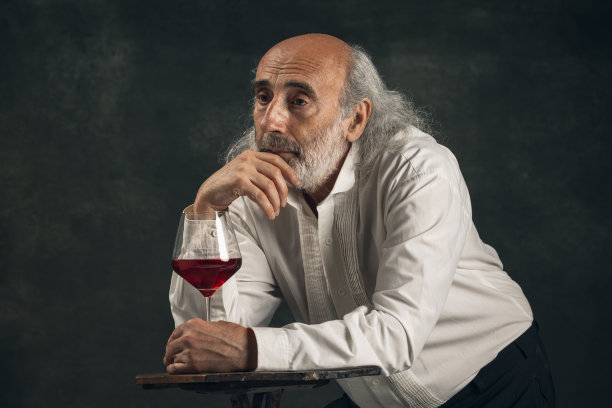 白发苍苍的老人，中世纪的历史人物，独饮暗色葡萄酒的演员。复古风格，比较时代的概念。图片下载