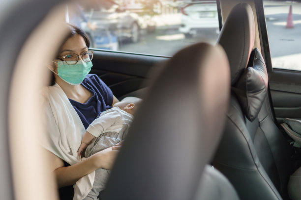 亚洲年轻母亲戴着防护面罩，抱着她的小男孩在车里。图片下载