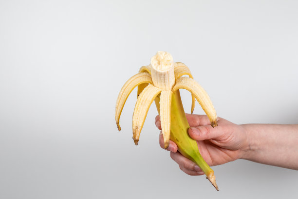 白色背景上，一个女人手里拿着被咬过的新鲜香蕉图片下载