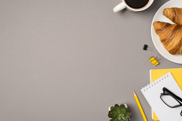 顶视图照片的杯咖啡盘子与两个新鲜的羊角面包，花盆眼镜，活页夹黄色铅笔和记事本在孤立的灰色背景与copyspace图片下载