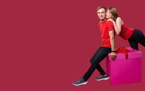 一个男朋友坐在一个系着蝴蝶结的大盒子上，他的女朋友把手放在她朋友的肩膀上。图片下载