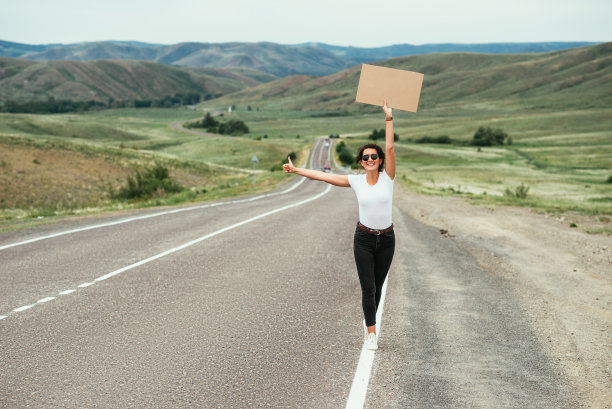 这个女孩在搭便车。一个女人在路上搭便车。在乡村公路上竖着大拇指搭车。旅行和搭便车的概念。漂亮的女孩旅行。本空间图片下载