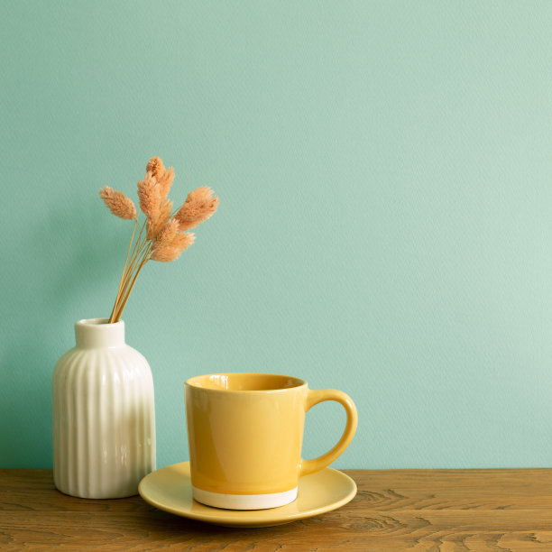 木桌上放着黄色的咖啡杯和粉红色的干花花瓶。薄荷墙背景。室内设计图片下载