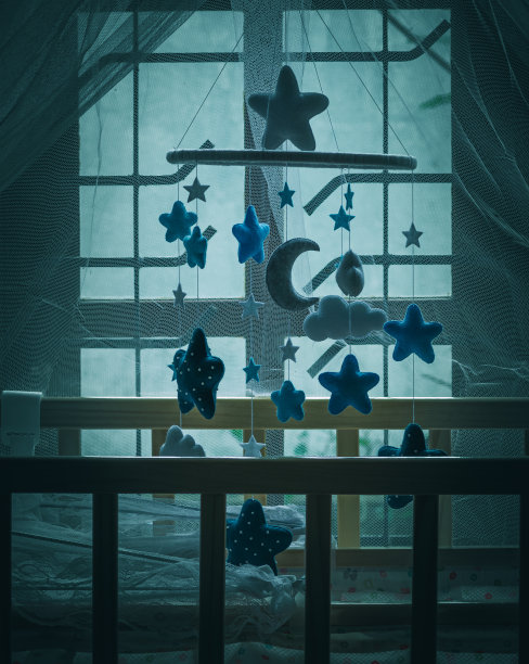 木制的婴儿床和悬挂的婴儿床移动在儿童卧室对着窗户的夜晚时间。图片下载