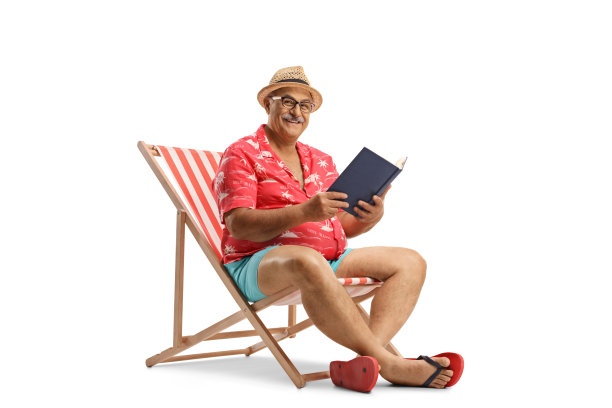 坐在沙滩椅上看书并看着镜头的年长男性游客图片下载