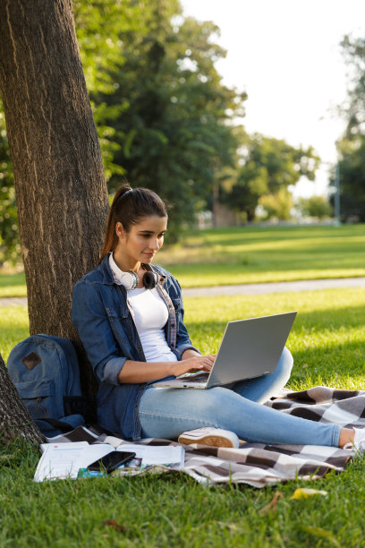 美丽的年轻女子学生在公园使用笔记本电脑。图片下载