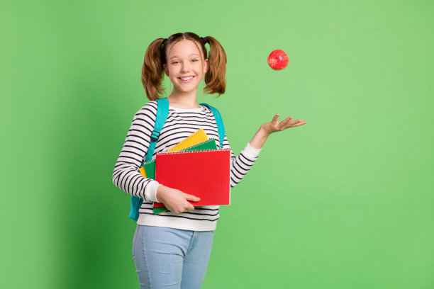 甜美可爱的学校女孩的照片穿白色套衫背包微笑打球孤立的绿色背景图片下载