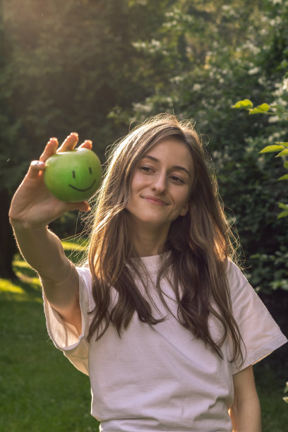 可爱的年轻女子手里拿着青苹果。新鲜的苹果。健康的食物和大自然中的人。迷人的年轻微笑的女人和水果在她的手。图片下载