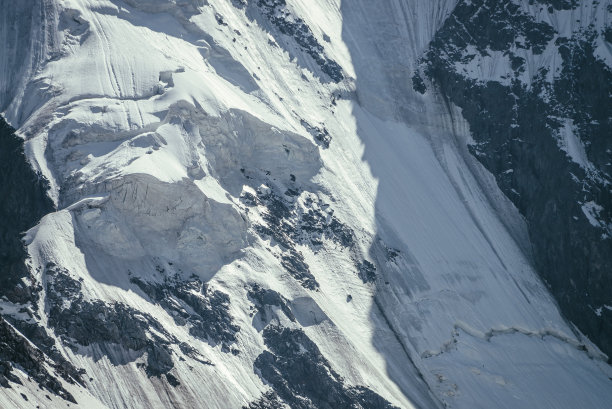 大岩石雪山墙的自然背景与白色冰川和雪檐口近距离。阳光下的雪山边，美丽的自然纹理。黑白色的高山的完整框架。图片下载