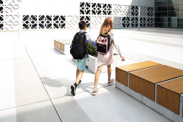 儿童、青少年、学童、男孩和女孩在混凝土墙的背景下，背着书包手牵着手去学校。从回来。回到学校图片下载