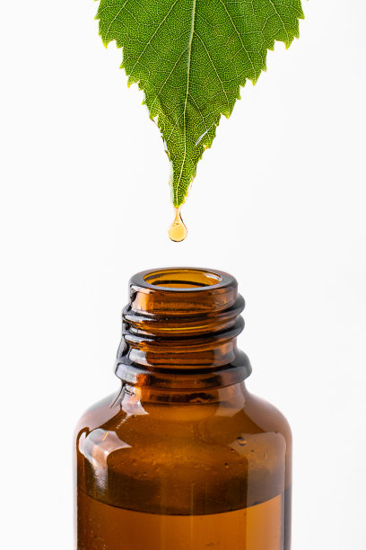 油滴从叶子滴到瓶孤立在白色的背景。图片下载