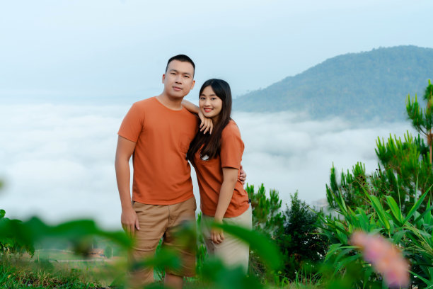 这是一对年轻的亚洲夫妇的肖像，他们穿着同样的棕色衬衫，在雾蒙蒙的早晨环境后面的一个美丽的旅游景点展示他们的爱。图片下载