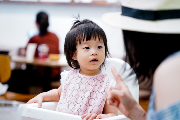 一个亚洲女婴在餐厅里听着她妈妈的讲话。图片下载