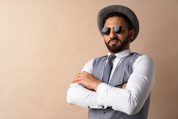 酷酷的埃及男子戴着帽子和太阳镜，在米色背景下摆姿势图片下载