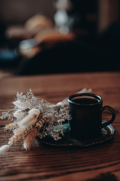 一张木桌上放着一杯黑咖啡和干花，背景模糊。图片下载