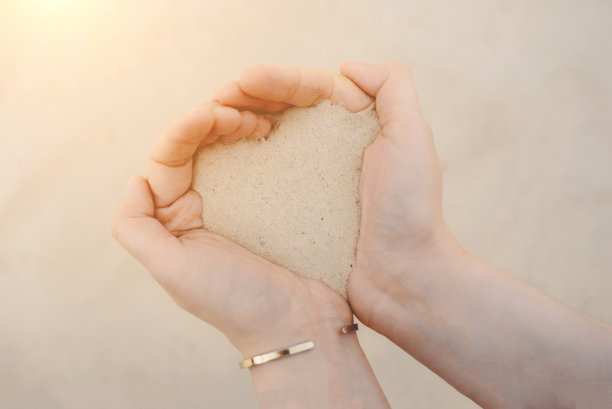 女人的双手捧着白色的沙滩沙子。图片下载
