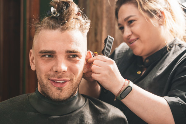 在理发店里，一个女发型师正在用理发钳给一个年轻的小伙子理发图片下载