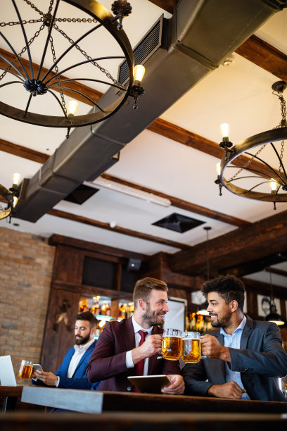 在酒吧休息的年轻商人们一边喝啤酒，一边谈笑风生图片下载