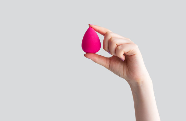 手握粉红色的蛋美丽海绵孤立在灰色的背景图片下载