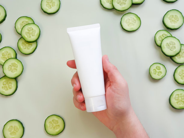 无品牌白色挤乳管在男人的手中。瓶子商标和新鲜黄瓜片浅绿色背景。俯视图，模型，模板。图片下载