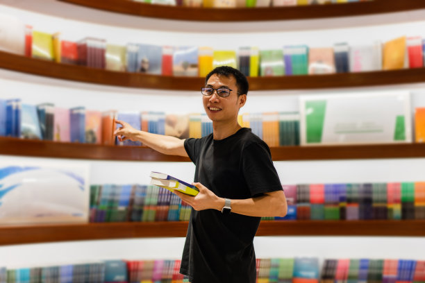 男人拿着两本书，手指指着书架上的书图片下载
