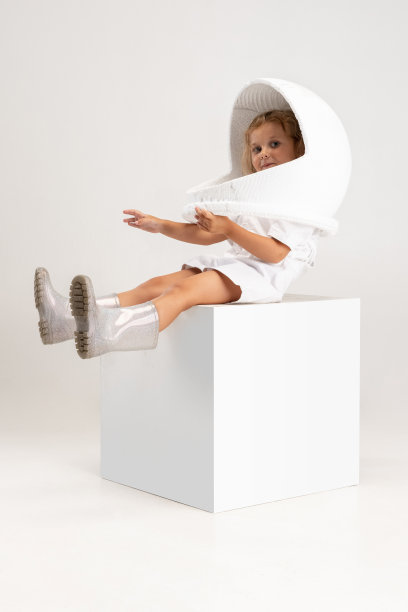 工作室拍摄的可爱的小学前班女孩在巨大的头盔姿势孤立的白色工作室背景。图片下载