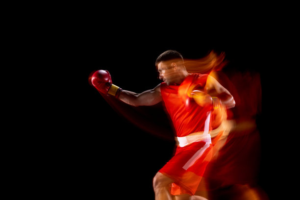 年轻的职业拳击手穿着红色短裤和手套训练，在混合灯光下的黑色背景下训练图片下载