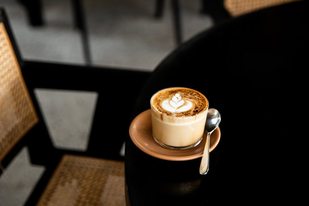 杯卡布奇诺，茶托上有拿铁图案，黑色的桌子上有勺子图片下载