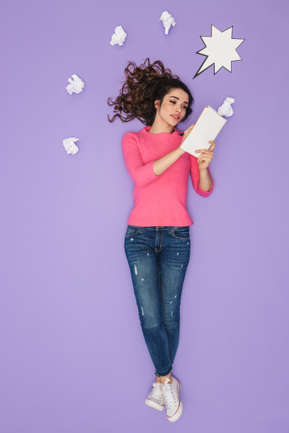 一名年轻女子的全身图像，她拿着纸笔记，在她的头部上方摆姿势表达想法或想法图片下载